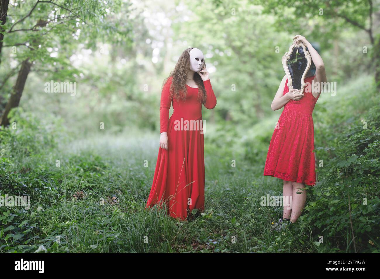 donne vestite di rosso con il viso coperto da una maschera e specchio vagante nel bosco, concetto fantasia Foto Stock