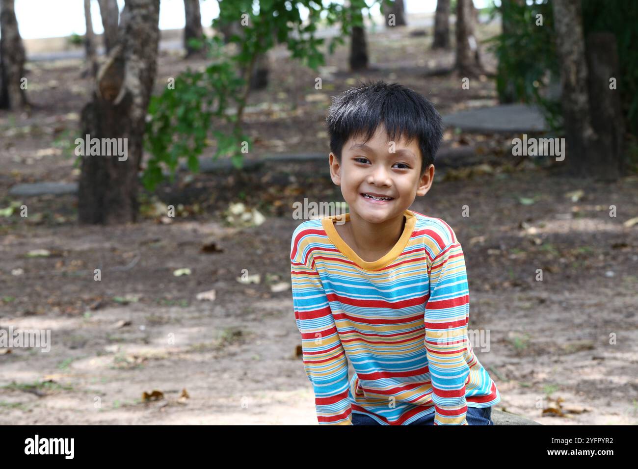 Un bambino gioioso siede in un parco, godendo della natura con un sorriso luminoso. La scena cattura l'essenza dell'esplorazione dell'infanzia e del gioco spensierato. Foto Stock