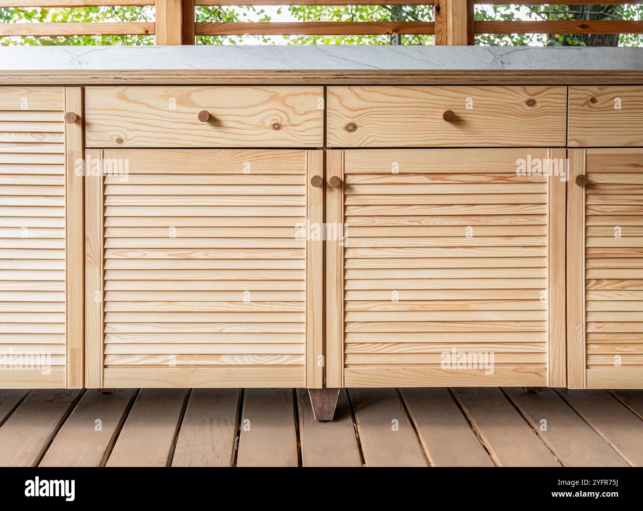 Armadi in legno di cucina esterna con porte a sfinestratura, cassetti, maniglie in legno e ripiani in compensato, si stendono su una terrazza in legno Foto Stock