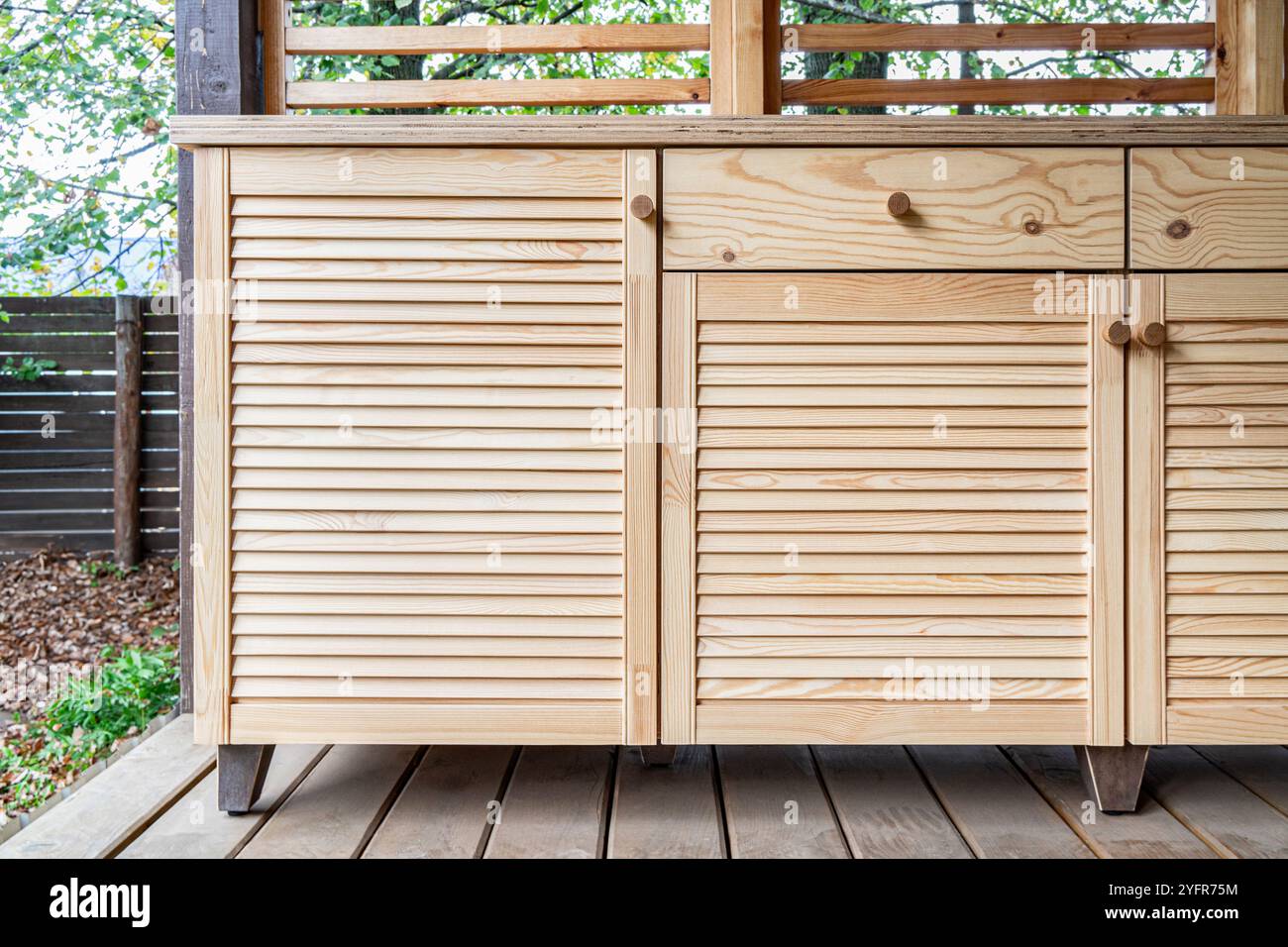 Armadi in legno di cucina esterna con porte a sfinestratura, cassetti, maniglie in legno e ripiani in compensato, si stendono su una terrazza in legno Foto Stock