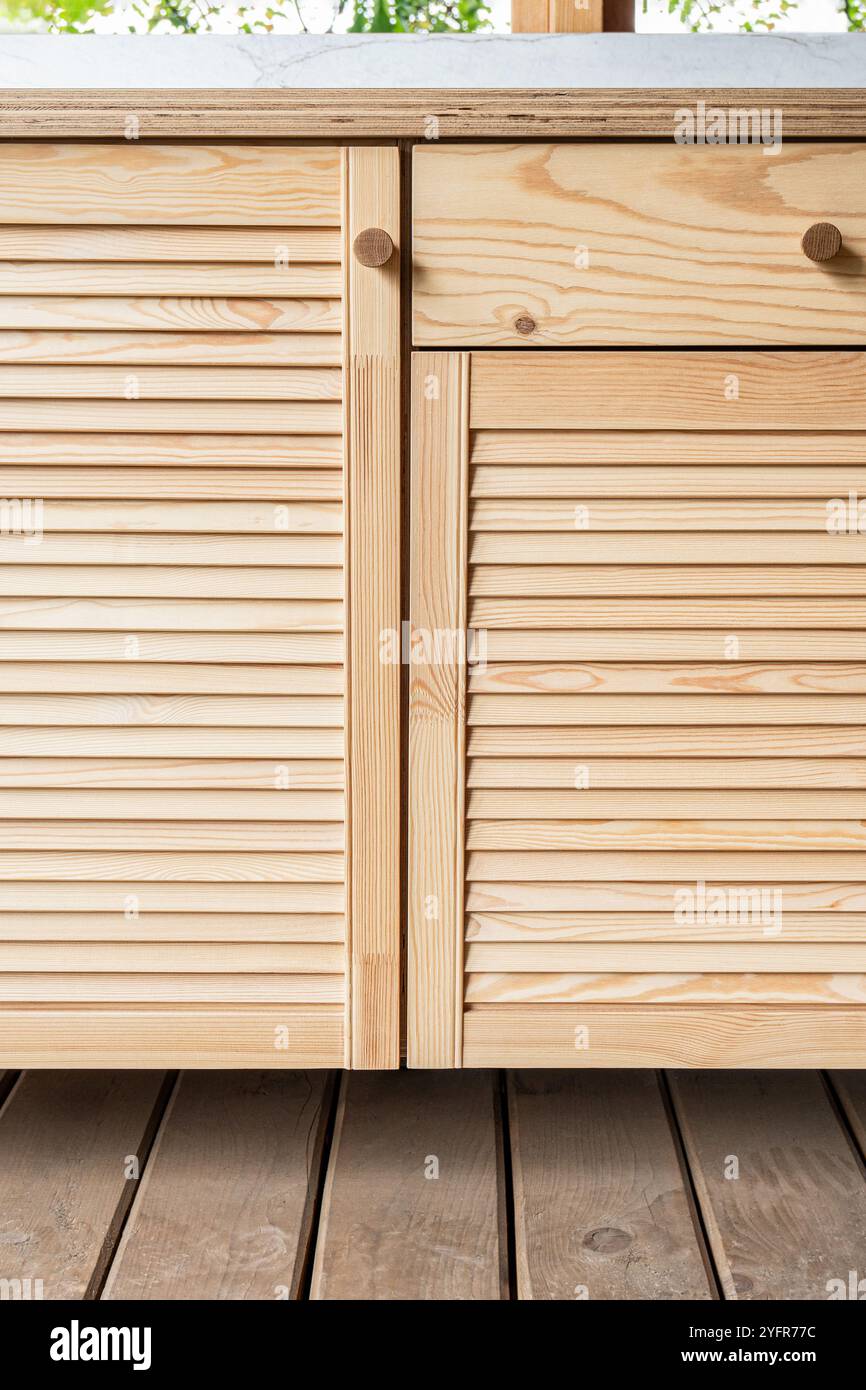 Armadi in legno di cucina esterna con porte a sfinestratura, cassetti, maniglie in legno e ripiani in compensato, si stagliano su una terrazza in legno vista ravvicinata Foto Stock