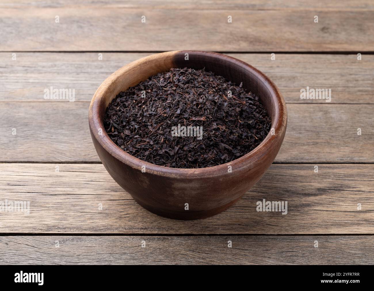 Foglie secche di tè nero su un recipiente sopra un tavolo di legno. Foto Stock