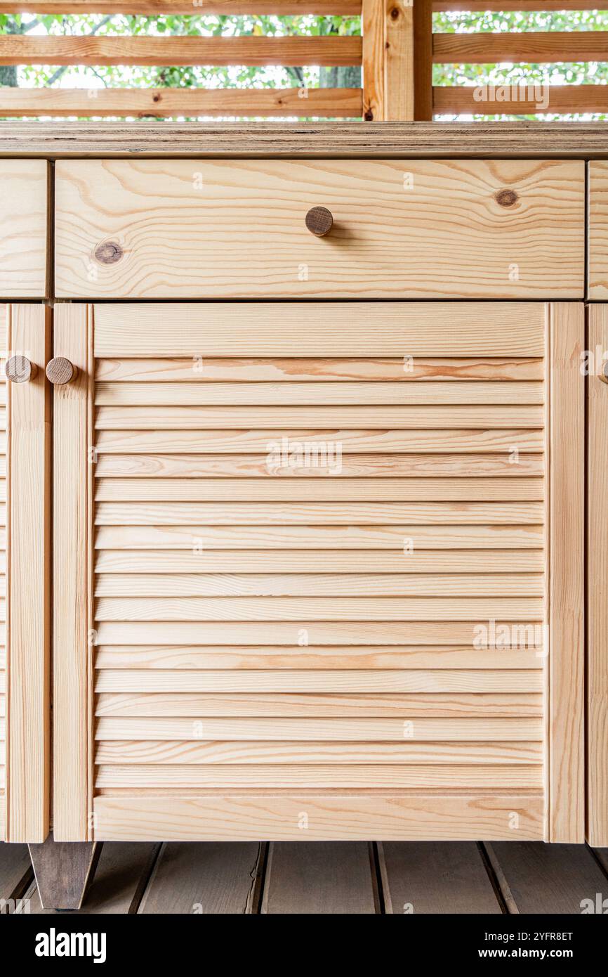Armadi in legno di cucina esterna con porte a sfinestratura, cassetti, maniglie in legno e un ripiano in compensato bianco si stagliano su una terrazza in legno vista ravvicinata Foto Stock