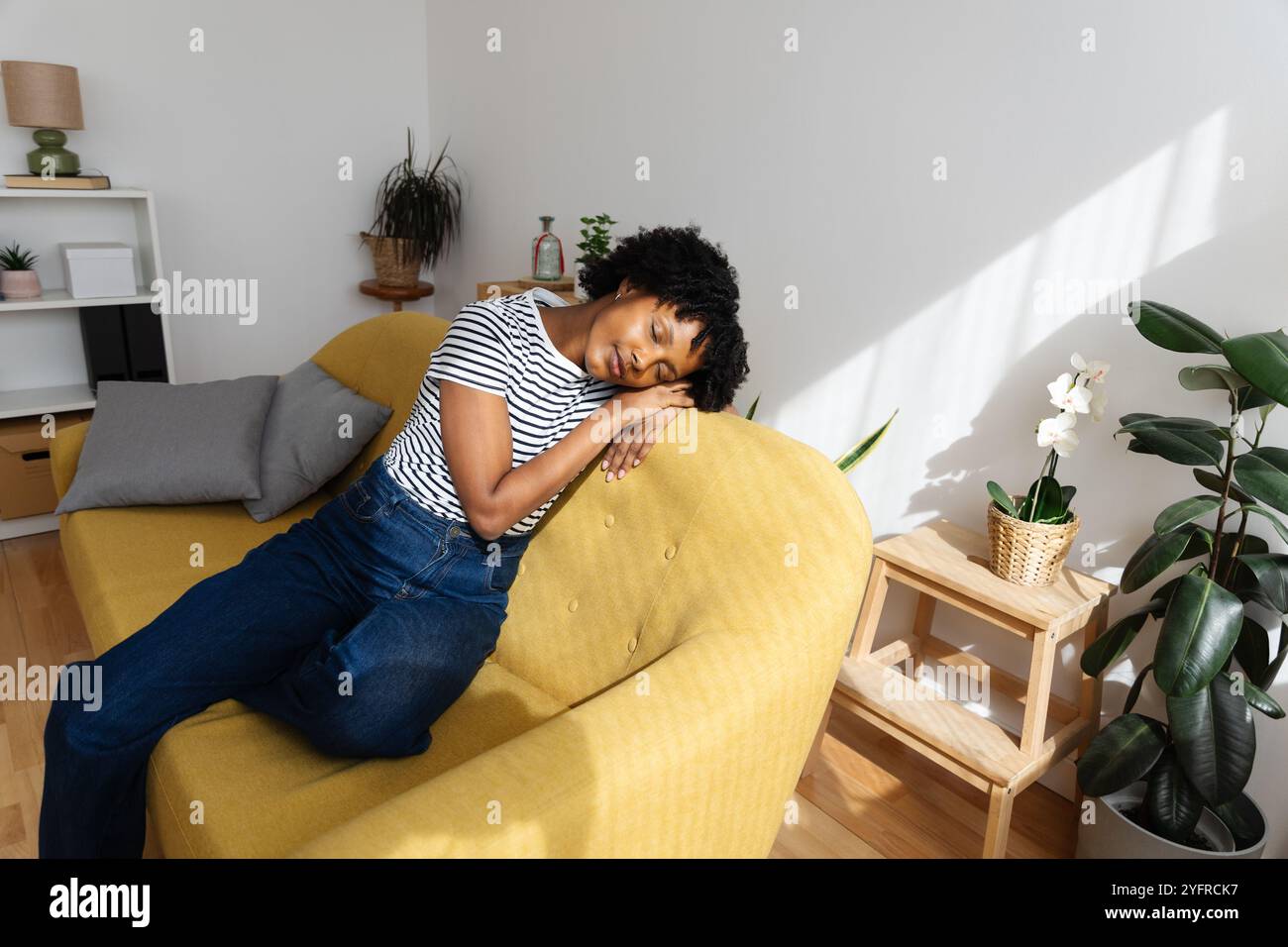 Una giovane ragazza afroamericana che fa un pisolino tranquillo sul divano giallo a casa Foto Stock