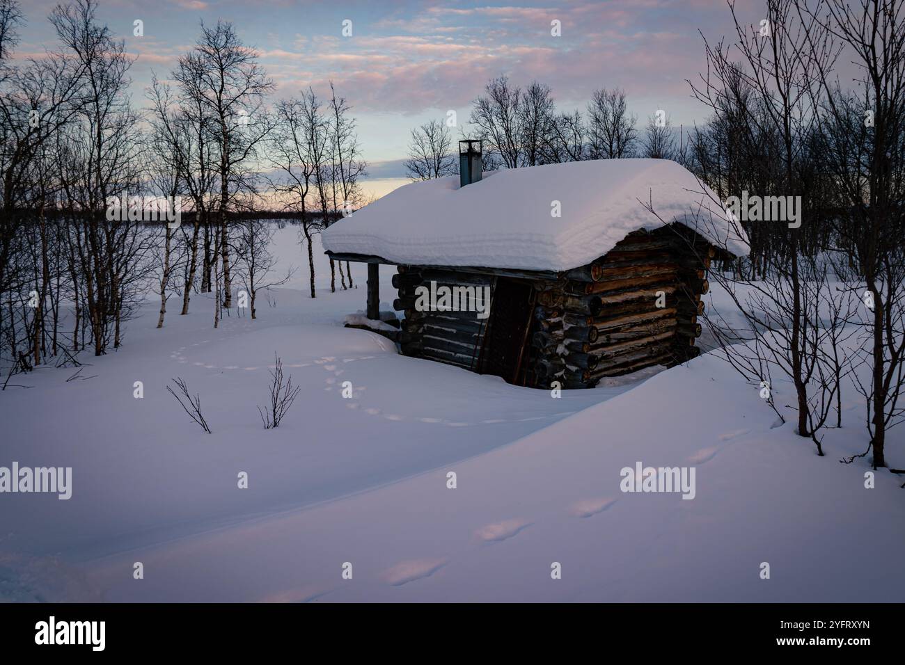 Capanna in legno selvaggio coperta di neve profonda al crepuscolo, cielo crepuscolo nel circolo polare artico finlandese, solitudine e tranquillità remote, tranquilla foresta innevata invernale Foto Stock