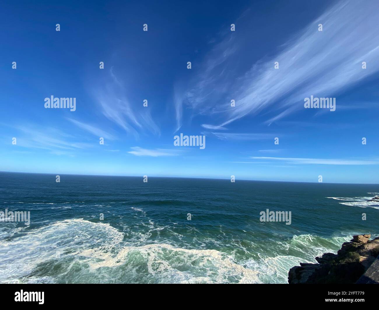 Cieli azzurri infiniti, nuvole morbide che spazzolano la superficie dell'oceano, la perfetta armonia della natura. Un momento di pace dove il mare incontra il cielo e il mondo si sente calmo Foto Stock