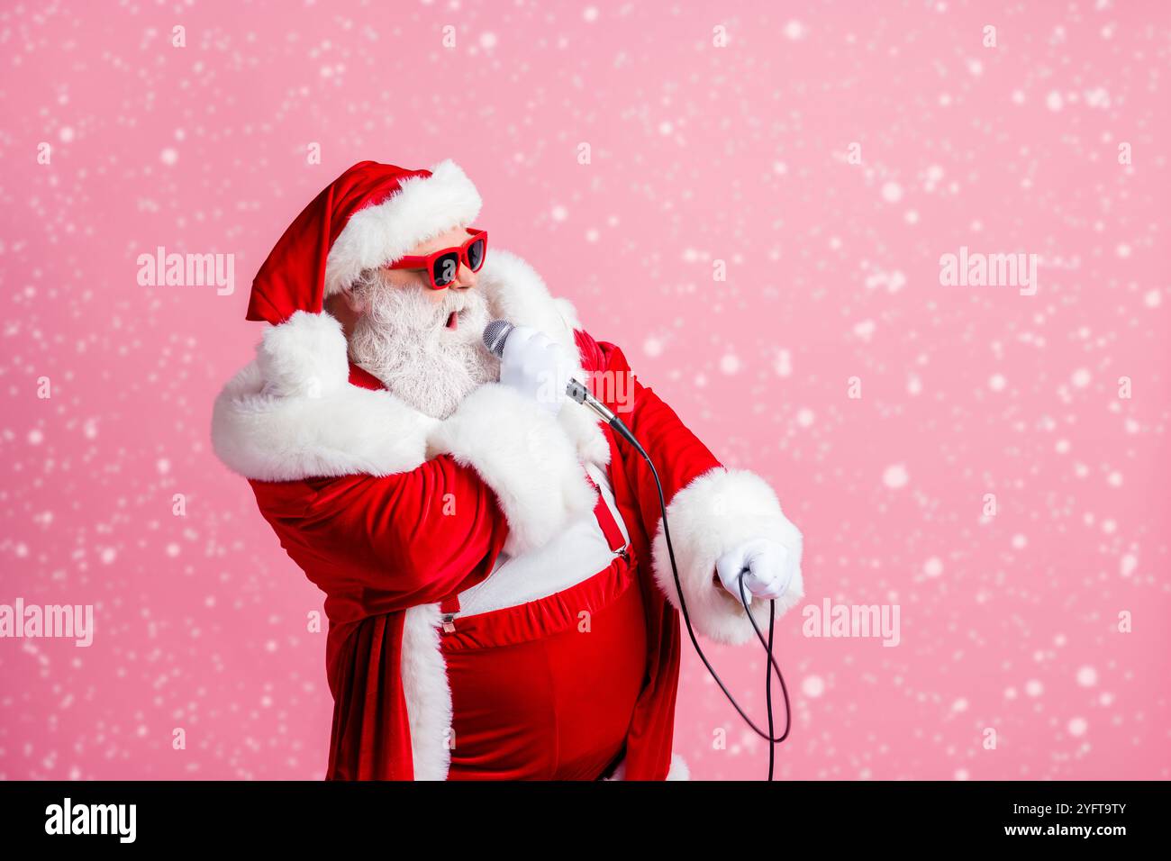 Profilo foto laterale di bianco grigio barba capelli funky pazzo babbo natale look copyspace cantare microfono x-mas canzoni di natale indossare sospenditori di usura della testa del cappuccio Foto Stock
