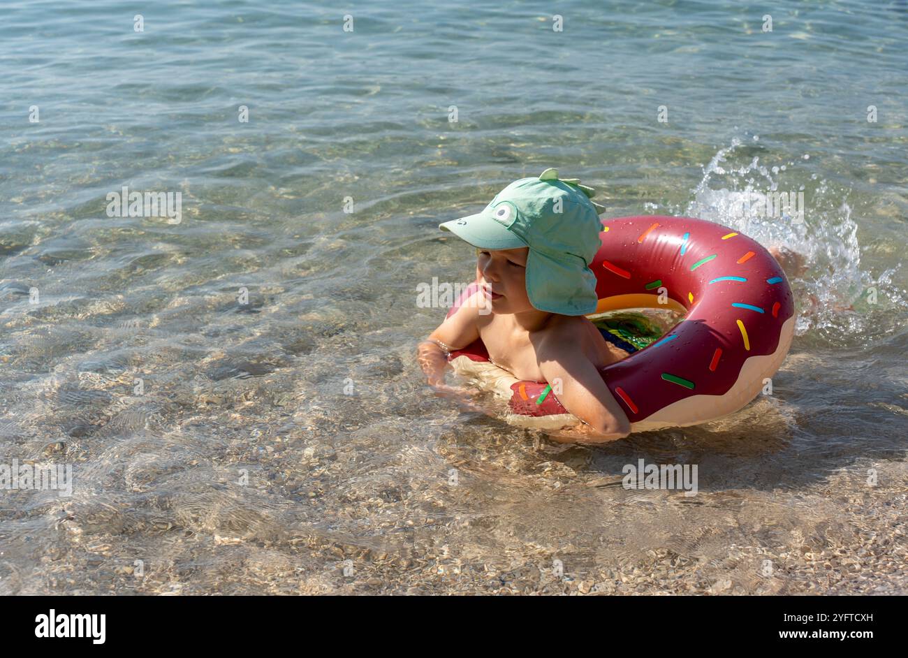 Il bambino in un anello gonfiabile a forma di ciambella gode di acque poco profonde nelle giornate di sole. Concetto di divertimento estivo, vacanza al mare e nuoto sicuro per i bambini Foto Stock