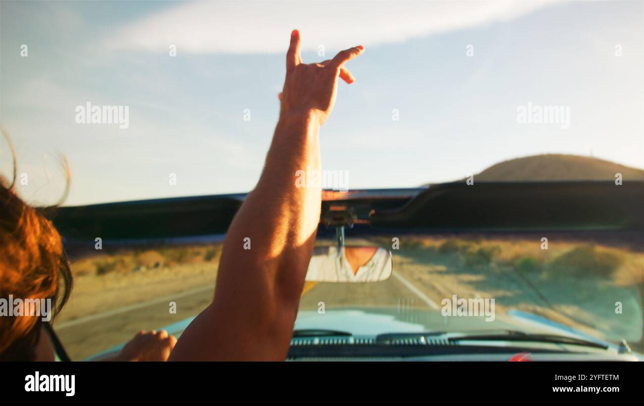 Primo piano di Man Driving Classic Open Top Car On Road viaggio attraverso la campagna con Hand in the Air Foto Stock