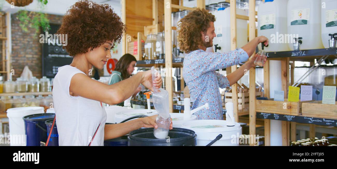 Donna che riempie il contenitore riutilizzabile con il prodotto per la pulizia in un negozio di alimentari senza plastica Foto Stock