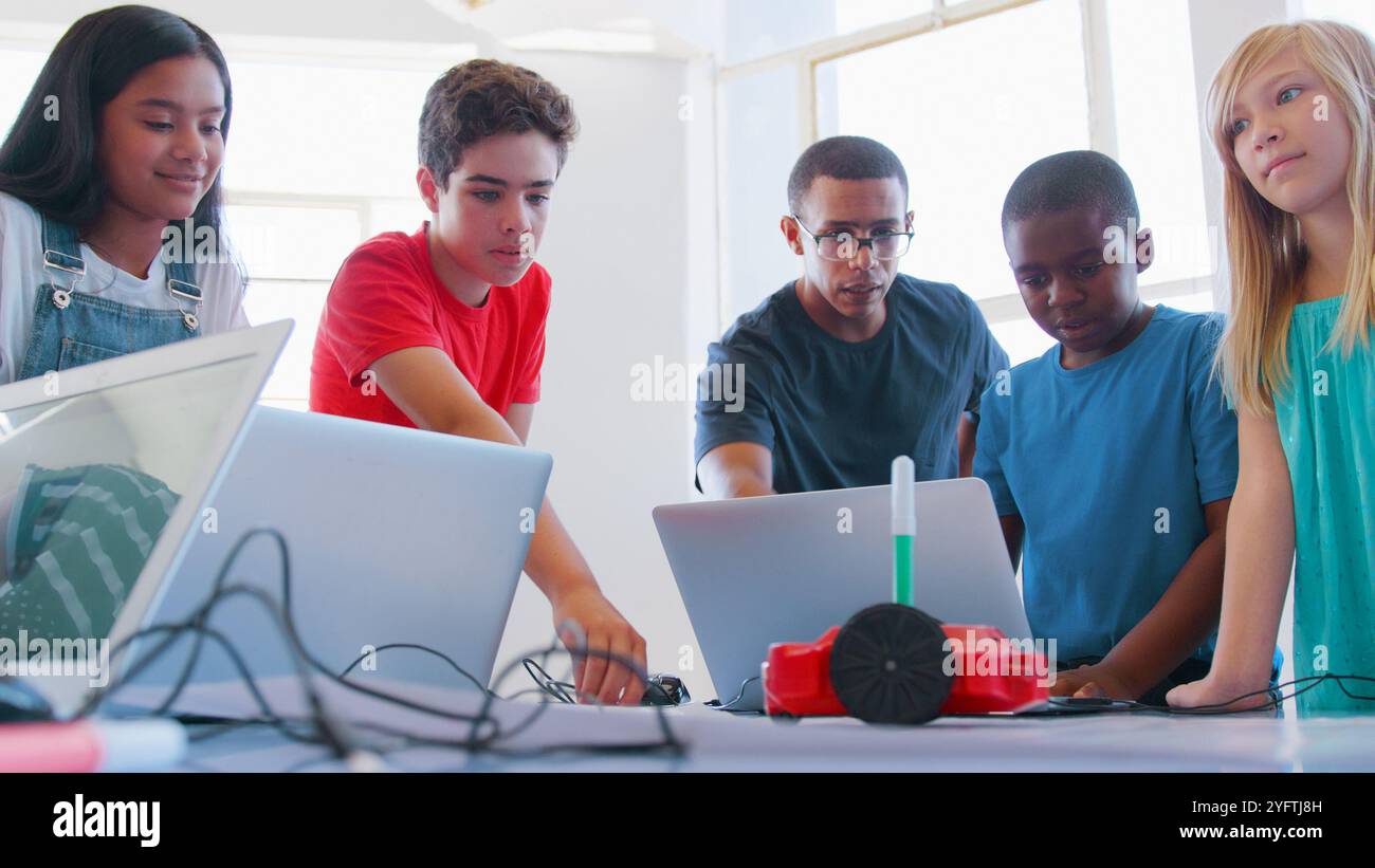 Gli studenti con insegnante maschile in classe di codifica dei computer scolastici imparano a programmare veicoli robot Foto Stock