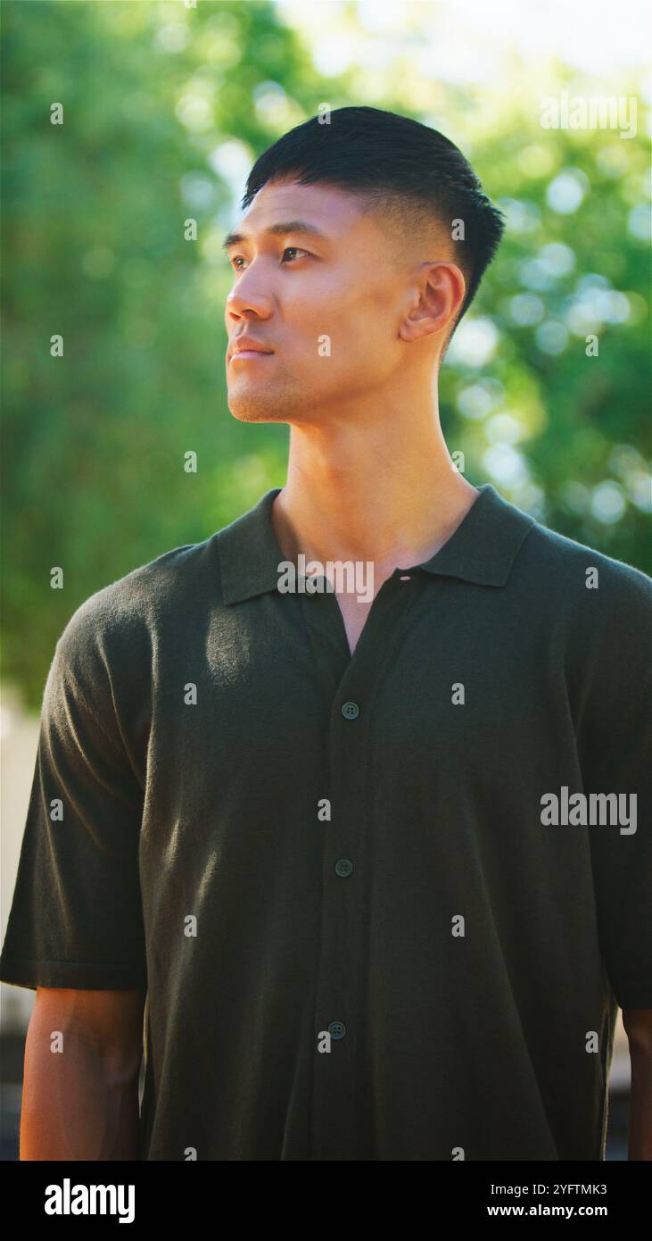 Un giovane uomo è in piedi all'aperto, guardando da un lato con un'espressione premurosa. La luce del sole illumina dolcemente il suo volto, evidenziando le sue caratteristiche Foto Stock