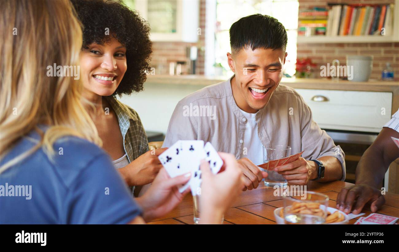 Un gruppo di amici è riunito intorno a un tavolo di legno, impegnato in un vivace gioco di carte. Le Risate riempiono l'aria mentre condividono spuntini e bevande, creando Foto Stock