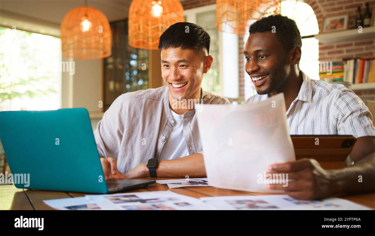 Due amici sono attivamente impegnati in un progetto creativo in uno spazio di lavoro interno ben illuminato. Stanno utilizzando un notebook, esaminando documenti e condividendo idee Foto Stock