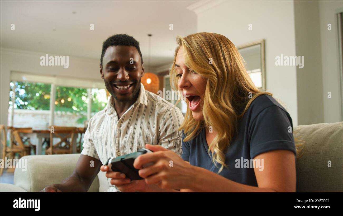 Due amici giocano eccitatamente ai videogiochi su un divano. Foto Stock