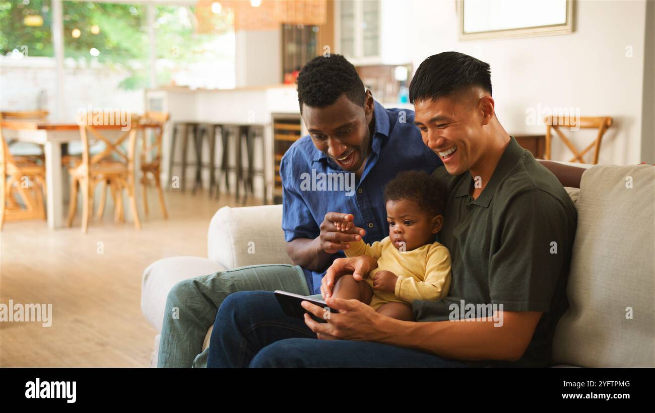 Due adulti e un bambino si divertono con un tablet, condividendo i sorrisi in uno spazio accogliente. Foto Stock