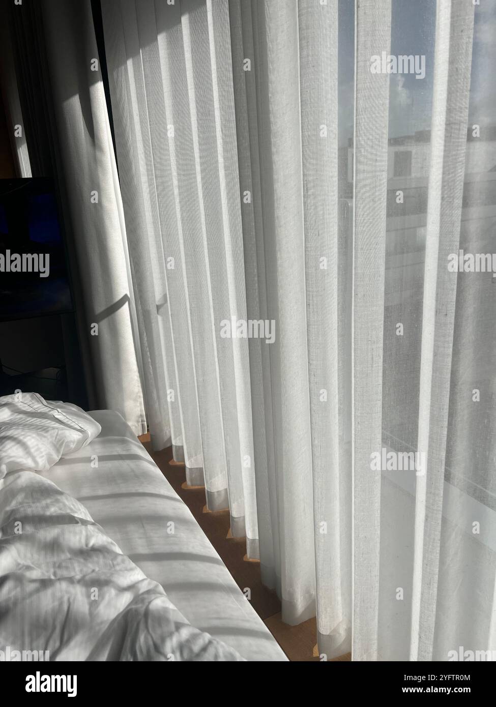 La luce soffusa del sole splende attraverso le tende bianche su un letto non realizzato, creando un'atmosfera tranquilla e calda Foto Stock