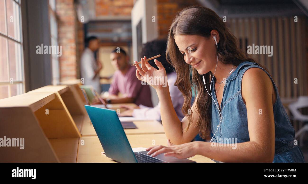 Donna d'affari che lavora in un moderno ufficio multiculturale ascoltando musica con auricolari o auricolari Foto Stock