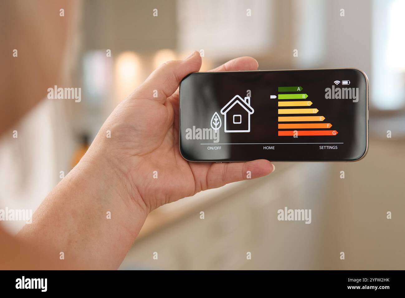 Una persona utilizza uno smartphone per monitorare i livelli di consumo energetico in un ambiente accogliente. Sul display viene visualizzato un grafico di efficienza energetica con variazioni Foto Stock