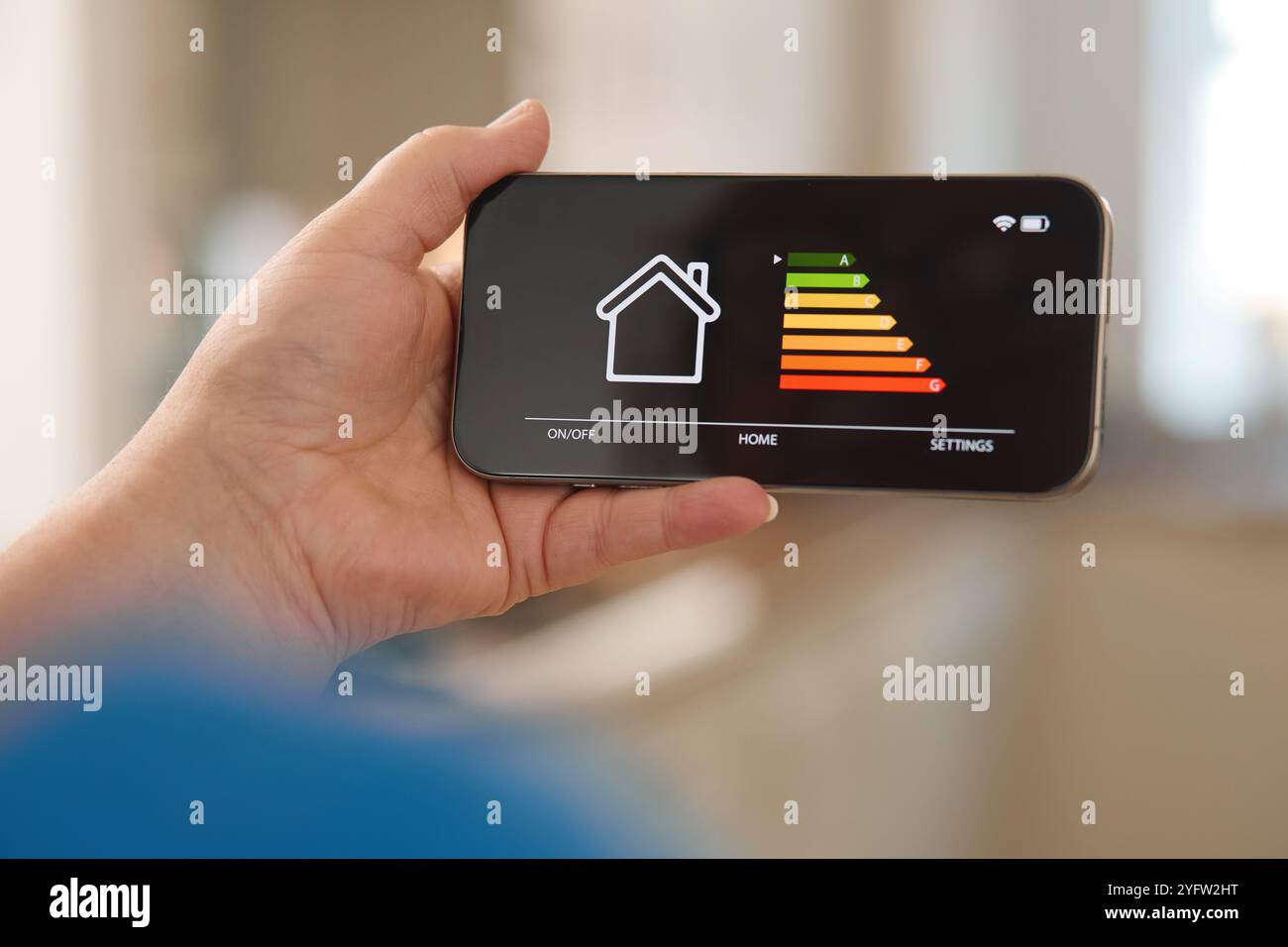 Una persona possiede uno smartphone che mostra un'interfaccia per l'automazione domestica, con i dettagli dei diversi livelli di energia indicati da barre colorate. Lo sfondo sugg Foto Stock