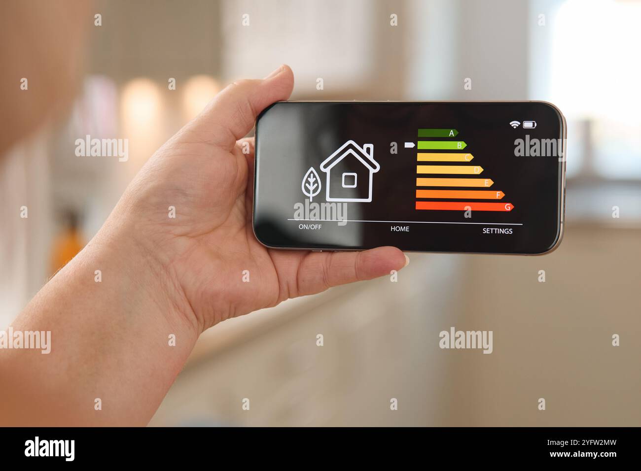 Una persona possiede uno smartphone che mostra un'interfaccia di gestione dell'energia per un sistema domestico intelligente. La schermata mostra una rappresentazione visiva di energ Foto Stock