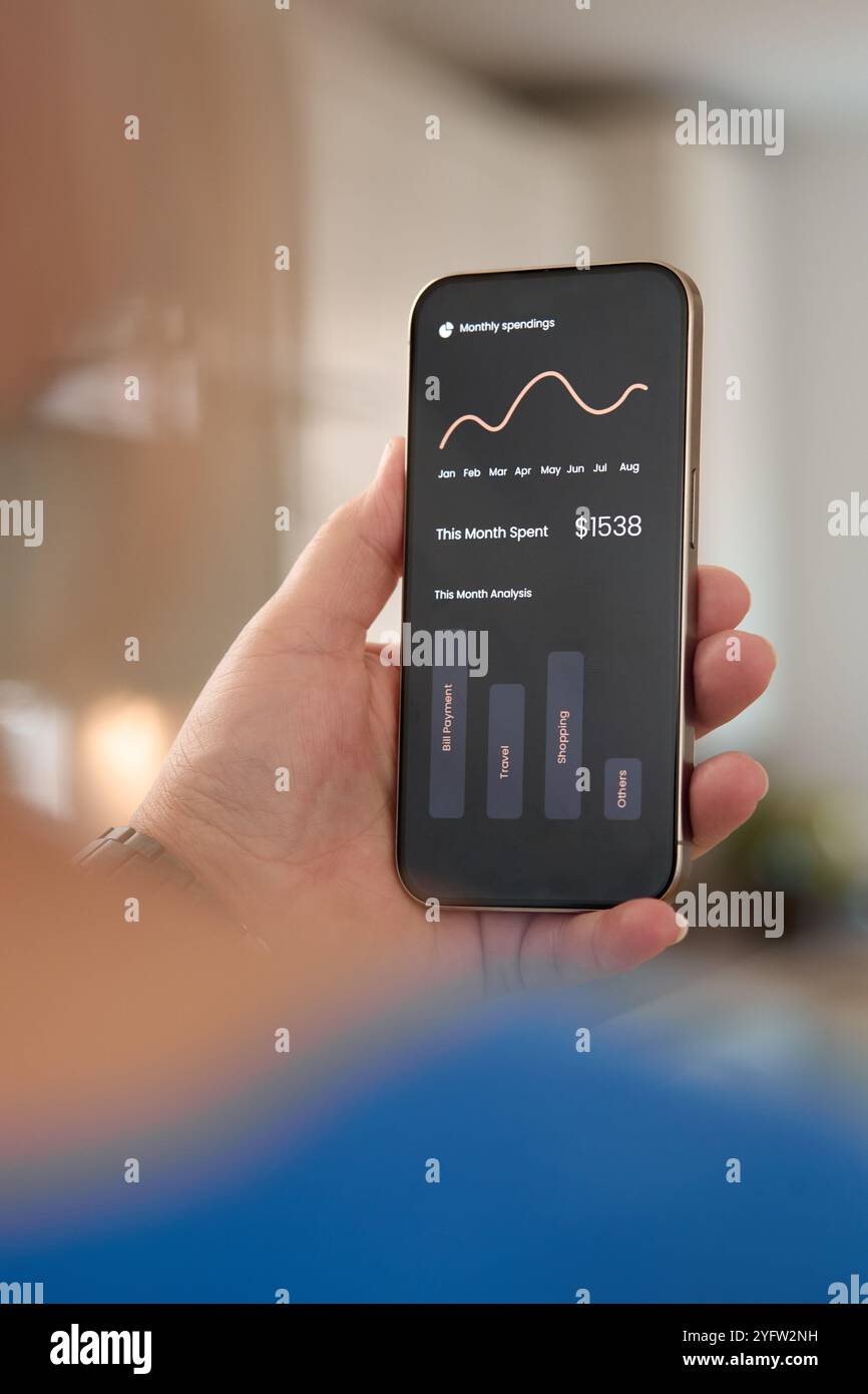 Una persona sta esaminando il proprio dashboard finanziario su uno smartphone, mostrando i guadagni e le tendenze mensili. L'ambiente sembra essere un ambiente accogliente Foto Stock