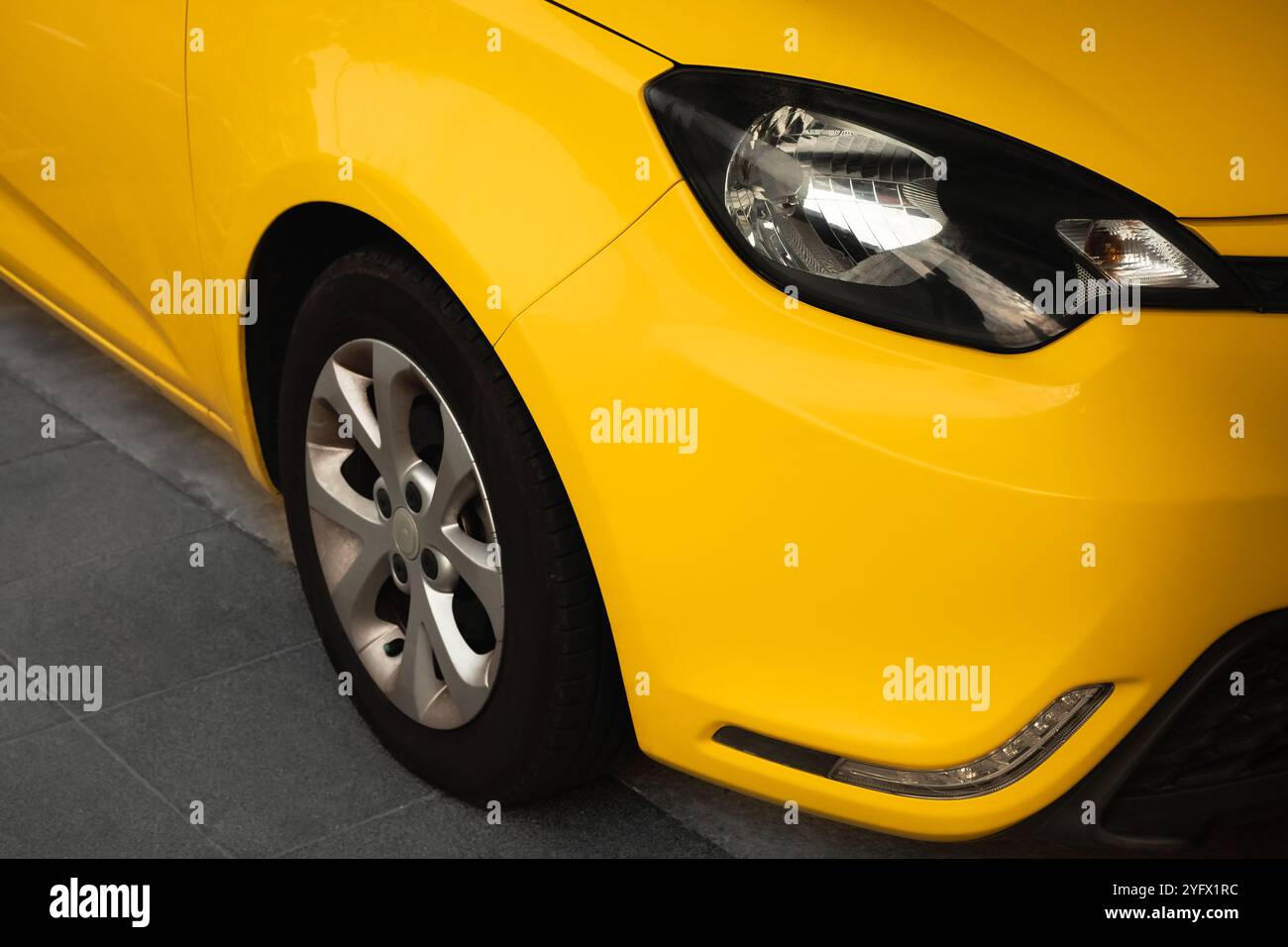 Fari e parte della ruota mostrati. Vista frontale della nuova e moderna auto gialla di lusso parcheggiata all'aperto. Fari e ruota di un'auto gialla Foto Stock