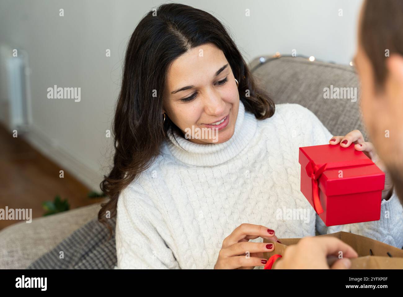 Bella donna bruna che riceve regali di Natale dal suo partner. Concetto di date di natale a casa con la famiglia Foto Stock
