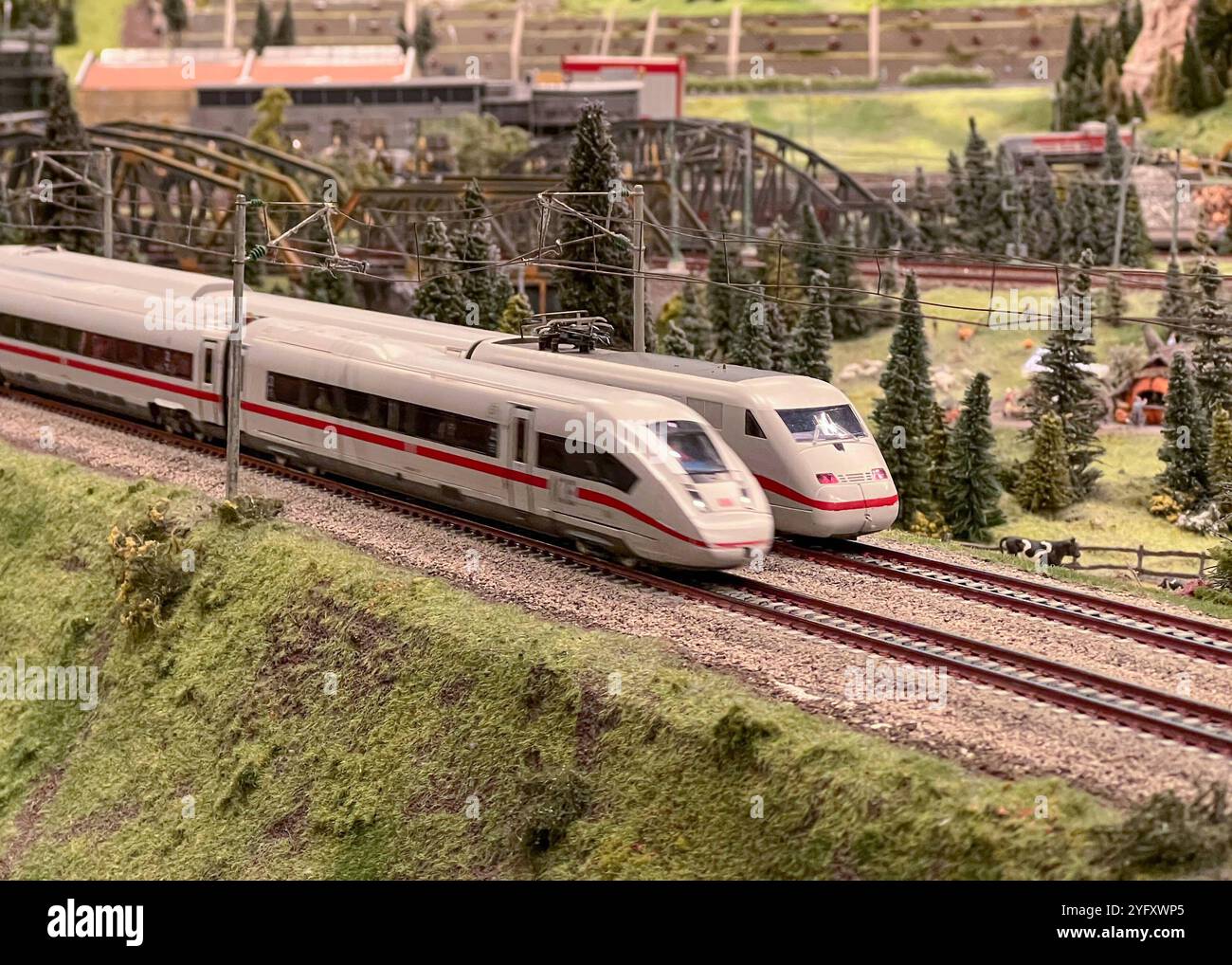 Symbolbild Zwei ICE-Züge auf parallelen Schienen im Miniaturformat, umgeben von Grüner Hügellandschaft und dichtem Wald, Brücken und weitere Bahngleise im Hintergrund, realistische Darstellung der Bahnstrecke, Oberleitungen und Strommasten für das Szenario, Felsen und Bäume sorgen ergänzen eine detailreiche Szenerie, Miniatur Wunderland und strommasten und Hochgeschwindigkeitszüge für Präzision Foto Stock