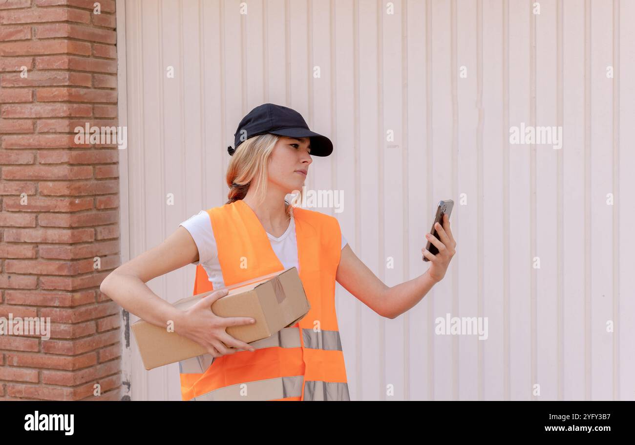 Una donna in consegna e' perduta a perquisire la casa per consegnare un pacco. Guarda il mobile concentrato. Città di ​​background. Foto Stock