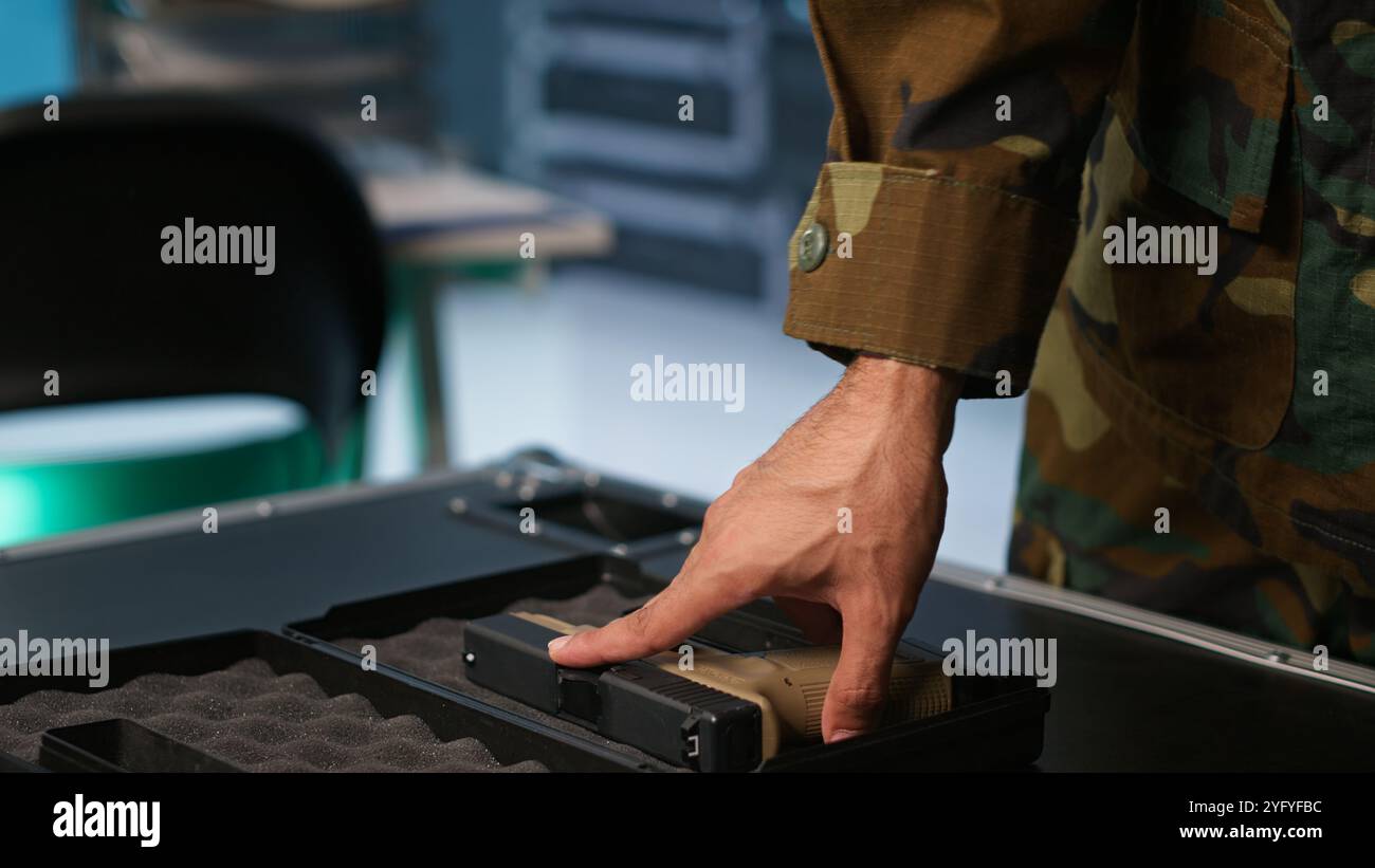 Ufficiale militare che controlla le pistole nella sala di comando, per assicurarsi che i proiettili e le forniture funzionino correttamente. Primo piano di un soldato che tiene in mano la pistola, gestisce le attrezzature di carico da combattimento, telecamera A. Foto Stock