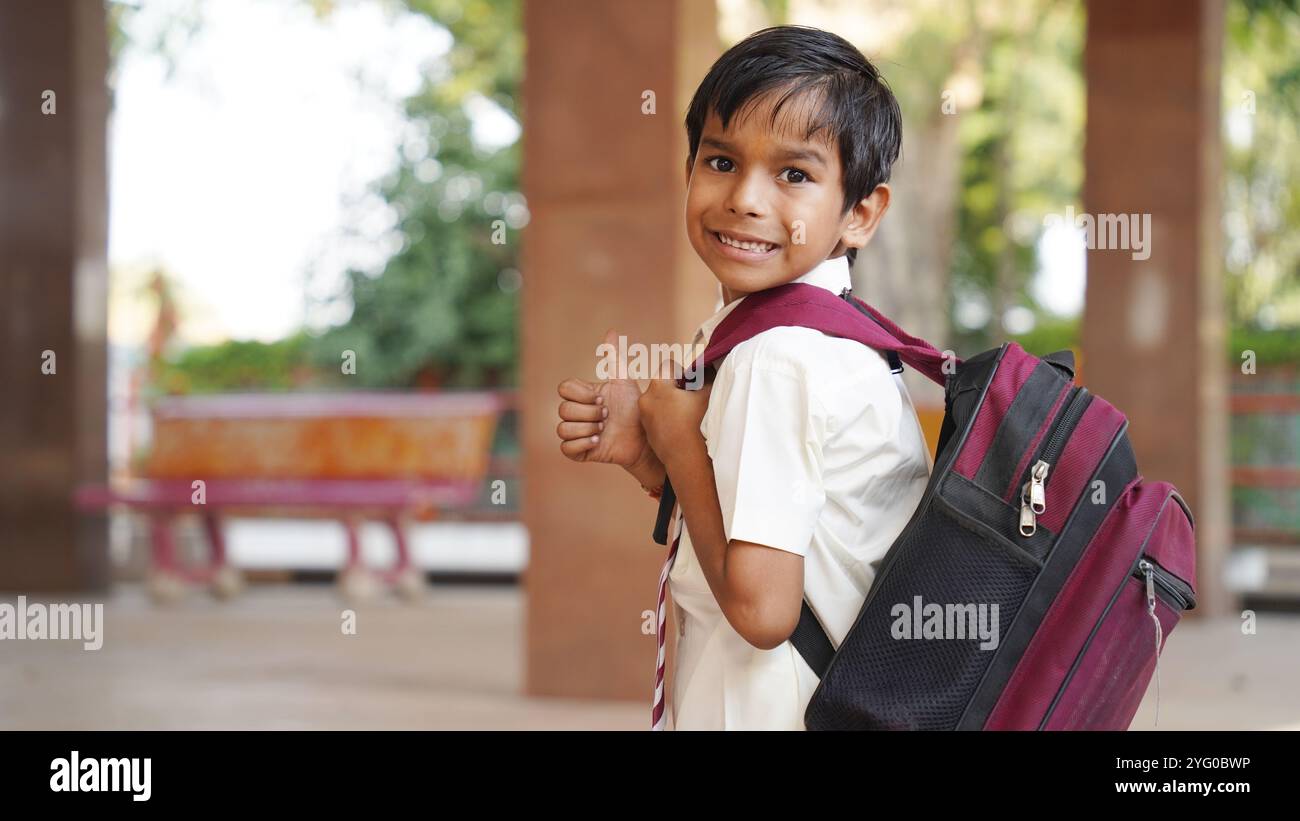 Sorridente ragazzo della scuola rurale indiana con lo zaino che guarda la macchina fotografica. Allegro ragazzo che indossa l'uniforme scolastica con un grande sorriso. Scuola elementare e elementare Foto Stock