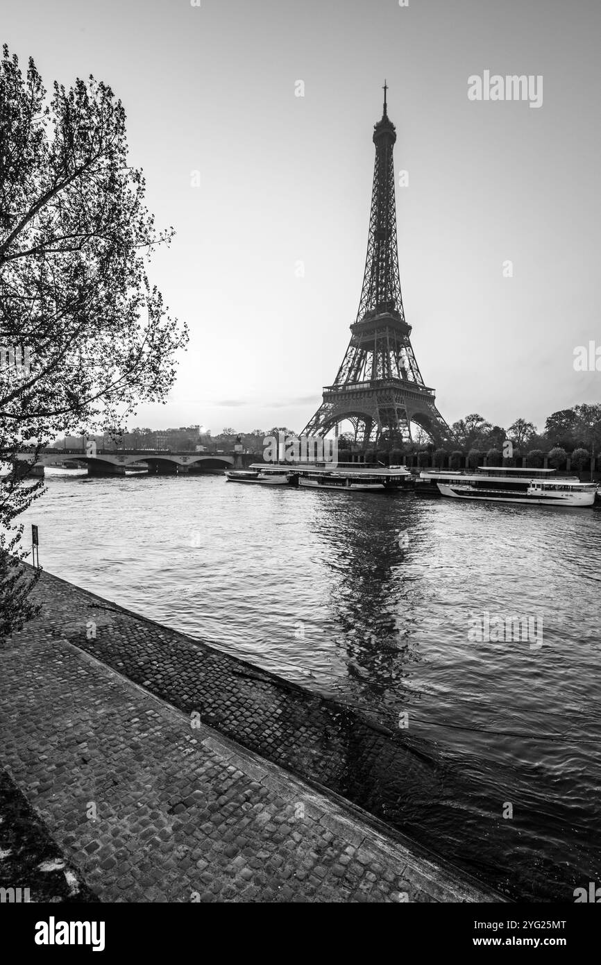 La Torre Eiffel si erge maestosamente mentre l'alba si rompe sulla Senna, proiettando un sereno riflesso sull'acqua, con la luce precoce che illumina lo skyline di Parigi. Foto Stock