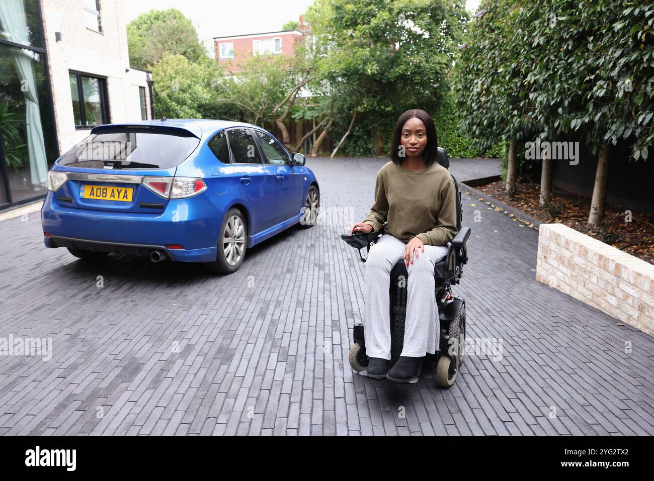 Donna seduta in sedia a rotelle sul vialetto, che guarda la macchina fotografica Foto Stock