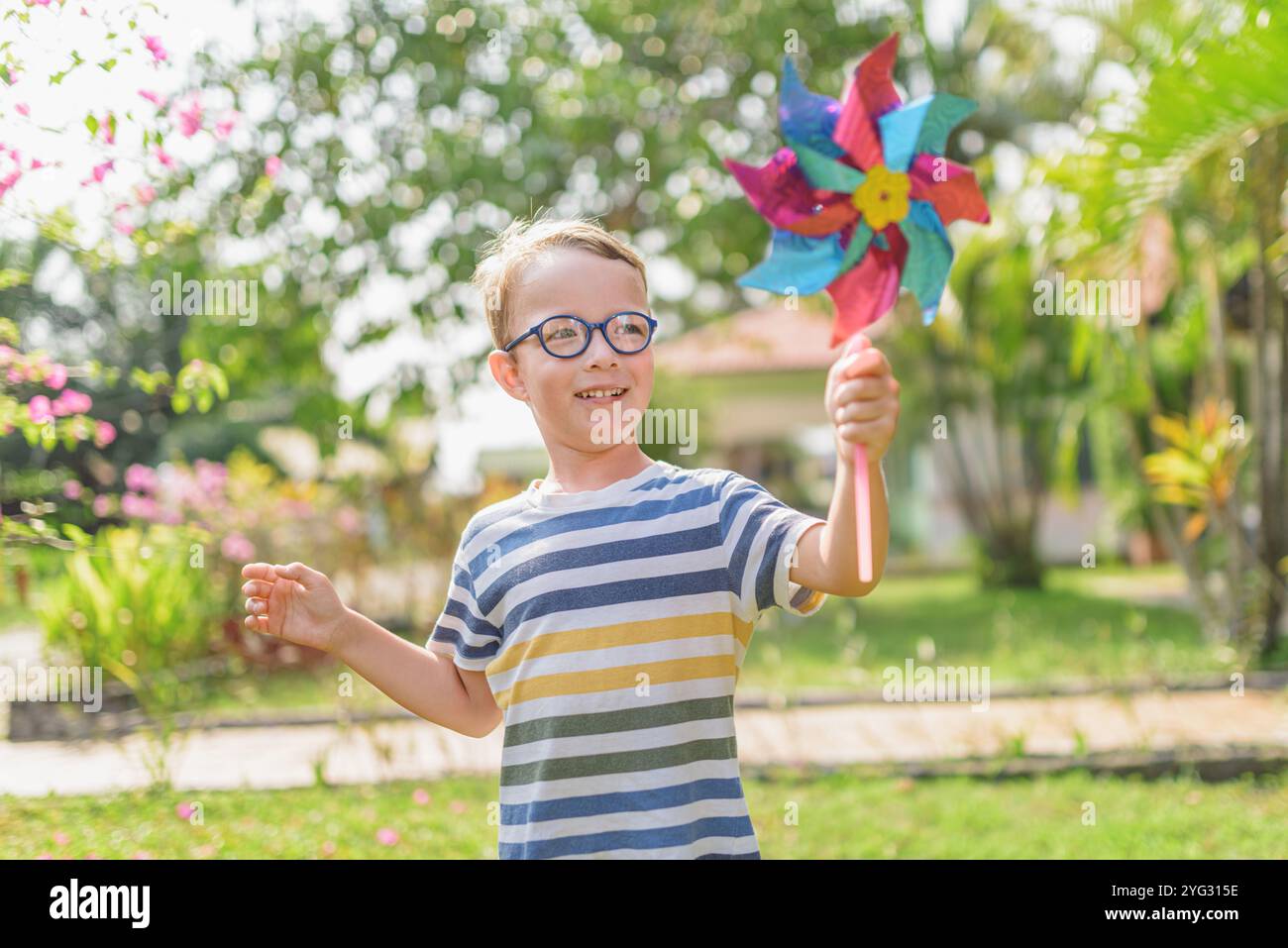 Il ragazzo con gli occhiali sta giocando con la ruota dentata in un giardino Foto Stock