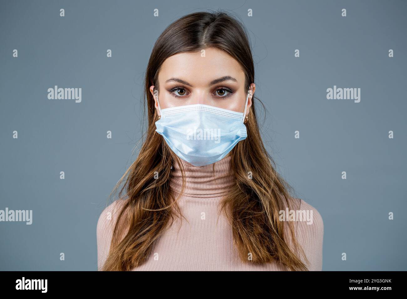 Donna che indossa una maschera medica. Donna che indossa la maschera chirurgica per il virus corona. Ragazza in maschera guardando da parte isolato sopra muro grigio Foto Stock