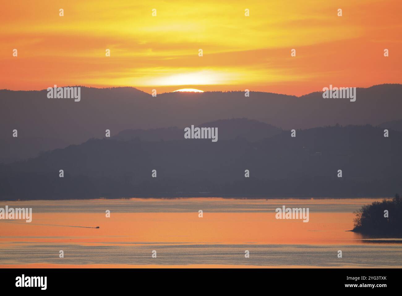 Tramonto dietro una catena montuosa lontana su un lago tranquillo, toni caldi, Hegne, Allensbach, lago di Costanza, Baden-Wuerttemberg, Germania, Europa Foto Stock