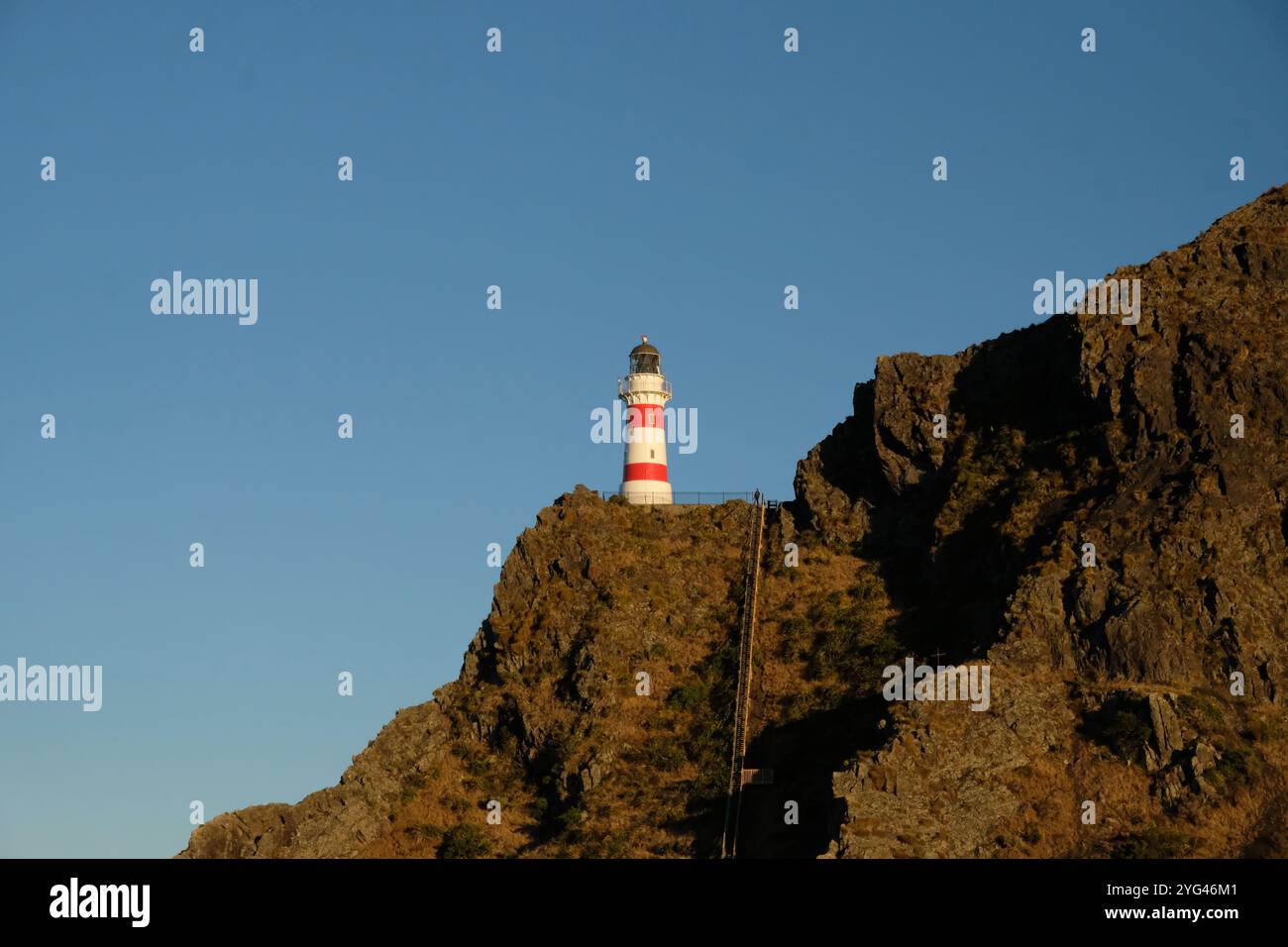 Pittoresco faro rosso e bianco durante il giorno su una scogliera che si affaccia su Cape Palliser, nuova Zelanda Foto Stock