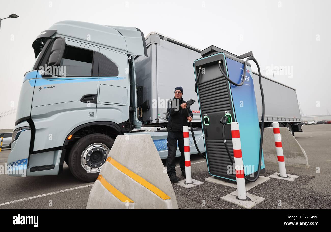 Amburgo, Germania. 6 novembre 2024. Rüdiger Düring, dipendente, si trova con un cavo di ricarica rapida su un camion elettrico "Iveco S-eway" vicino a una stazione di ricarica in occasione di un evento stampa per l'apertura di un hub di ricarica per camion elettrici presso il Cruise Center Steinwerder nel porto di Amburgo. Credito: Christian Charisius/dpa/Alamy Live News Foto Stock