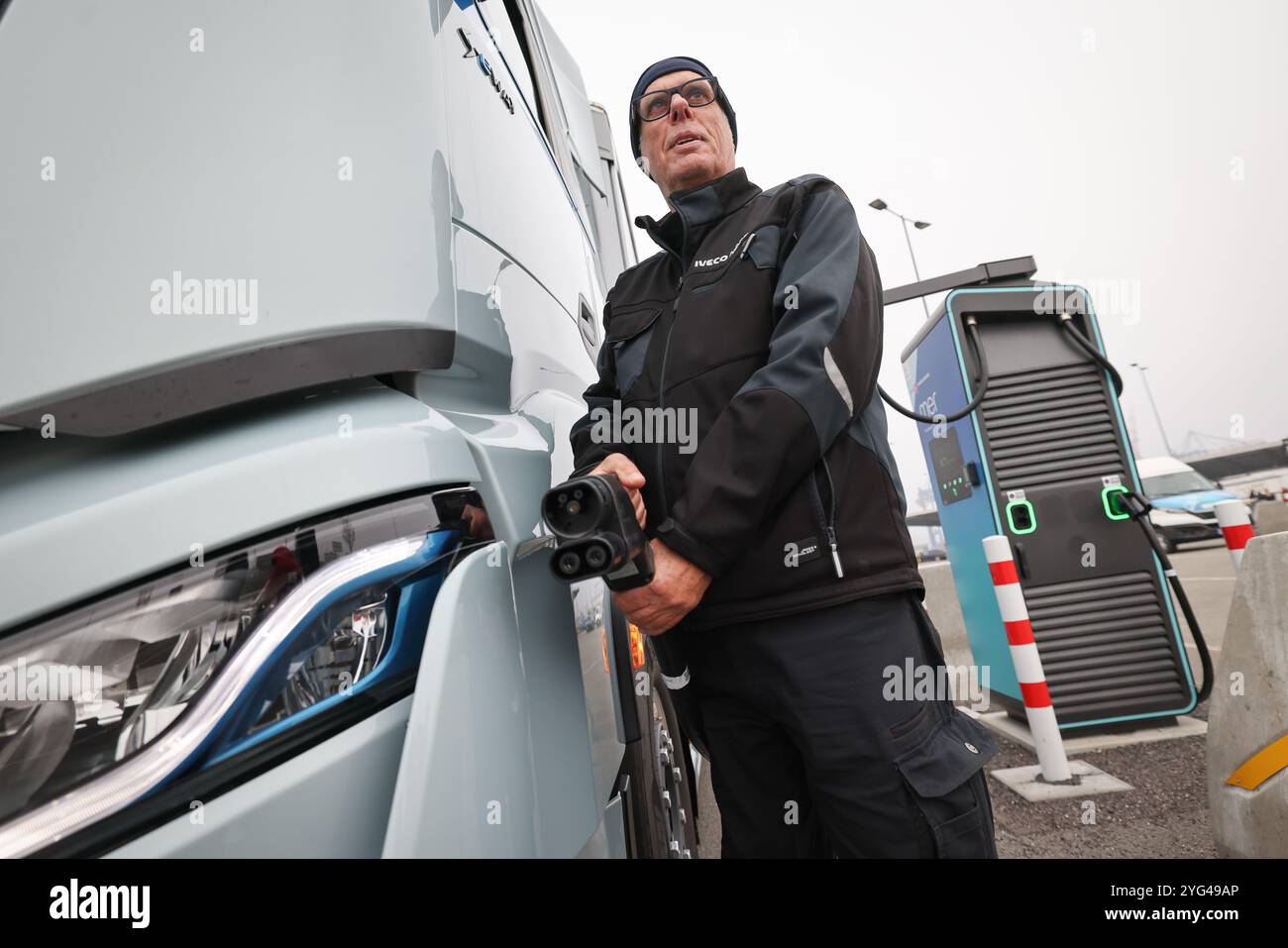 Amburgo, Germania. 6 novembre 2024. Rüdiger Düring, dipendente, si trova con un cavo di ricarica rapida su un camion elettrico "Iveco S-eway" vicino a una stazione di ricarica in occasione di un evento stampa per l'apertura di un hub di ricarica per camion elettrici presso il Cruise Center Steinwerder nel porto di Amburgo. Credito: Christian Charisius/dpa/Alamy Live News Foto Stock