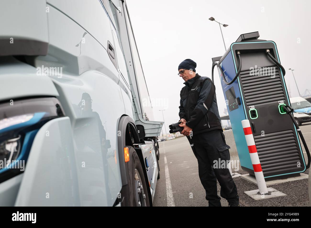 Amburgo, Germania. 6 novembre 2024. Rüdiger Düring, dipendente, si trova con un cavo di ricarica rapida su un camion elettrico "Iveco S-eway" vicino a una stazione di ricarica in occasione di un evento stampa per l'apertura di un hub di ricarica per camion elettrici presso il Cruise Center Steinwerder nel porto di Amburgo. Credito: Christian Charisius/dpa/Alamy Live News Foto Stock