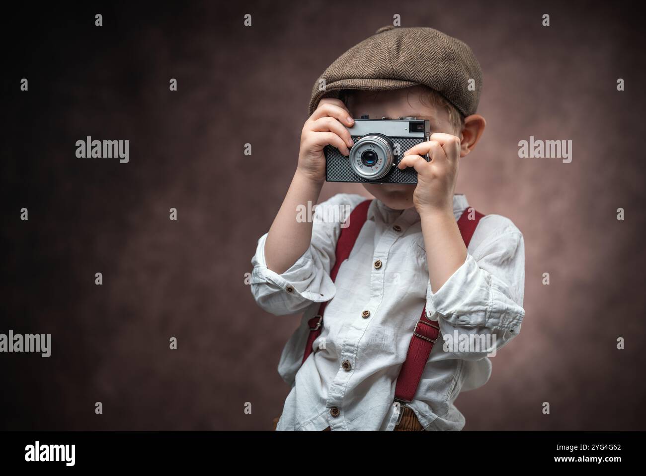 Fotografo ragazzo con fotocamera retrò che crea immagini su sfondo vintage Foto Stock