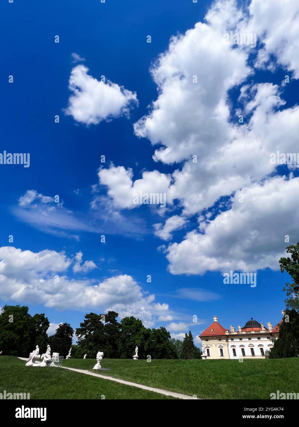 Una splendida immagine di uno storico palazzo europeo circondato da una vibrante vegetazione e da un cielo blu luminoso con soffici nuvole a Slavkov u Brna, Repubblica Ceca Foto Stock