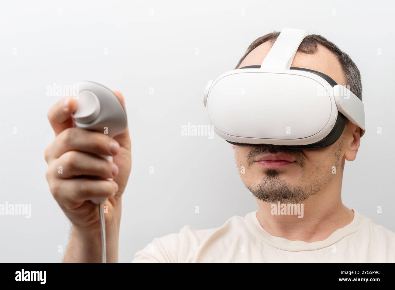 L'uomo si impegna con il visore per la realtà virtuale, concentrandosi sull'esperienza immersiva tenendo il controller in mano. Foto Stock