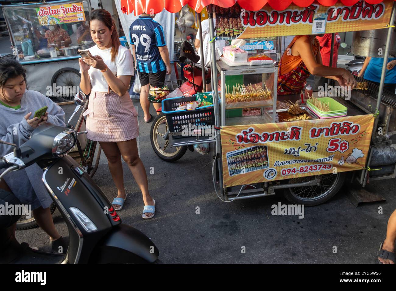 SAMUT PRAKAN, TAILANDIA, 16 GIUGNO 2024, la gente aspetta in un chiosco di strada che offre carne alla griglia, nel tardo pomeriggio Foto Stock