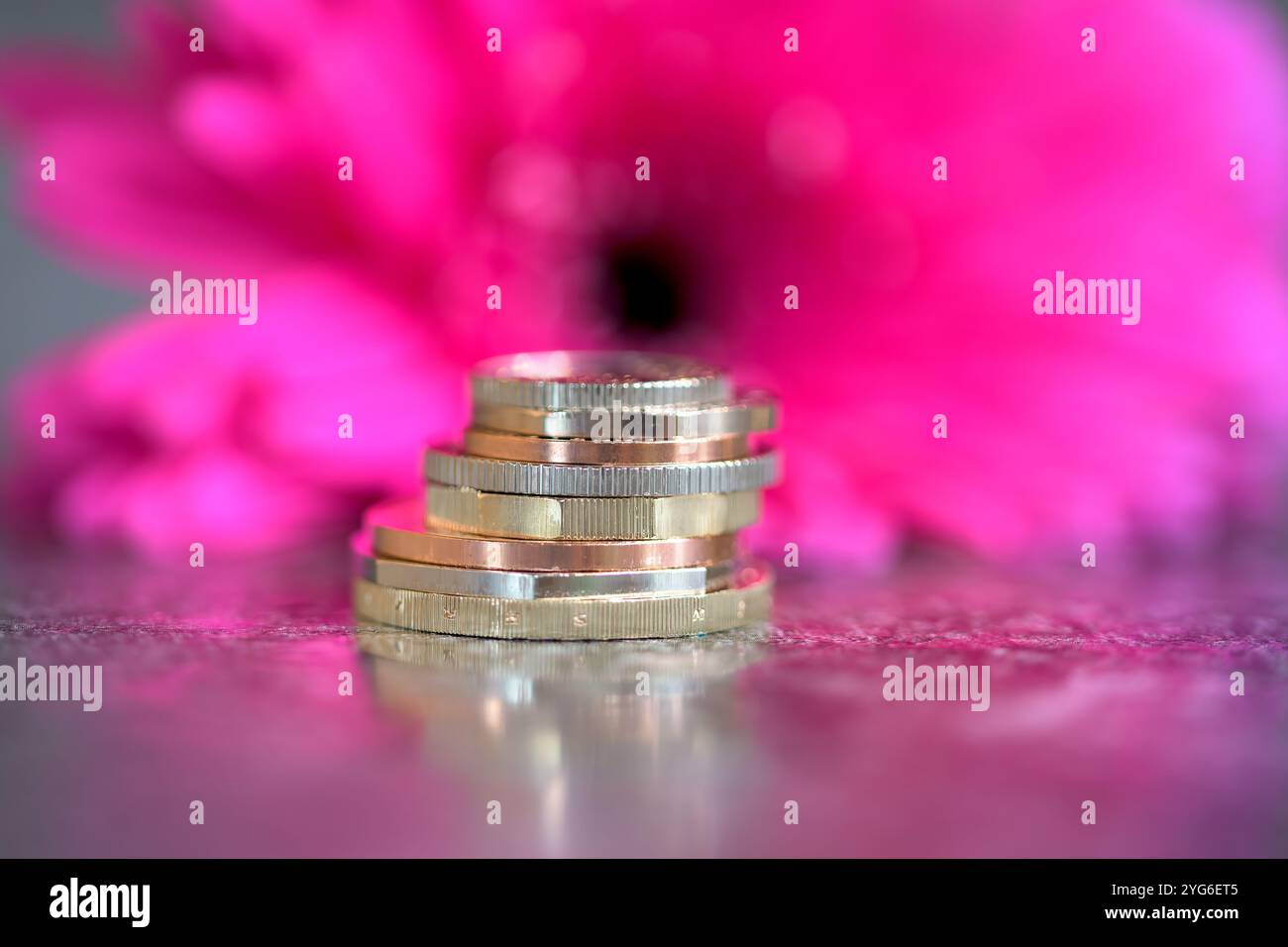 Un'immagine focalizzata di una pila di monete con un vivace sfondo rosa sfocato che simboleggia prosperità, risparmi e successo finanziario Foto Stock