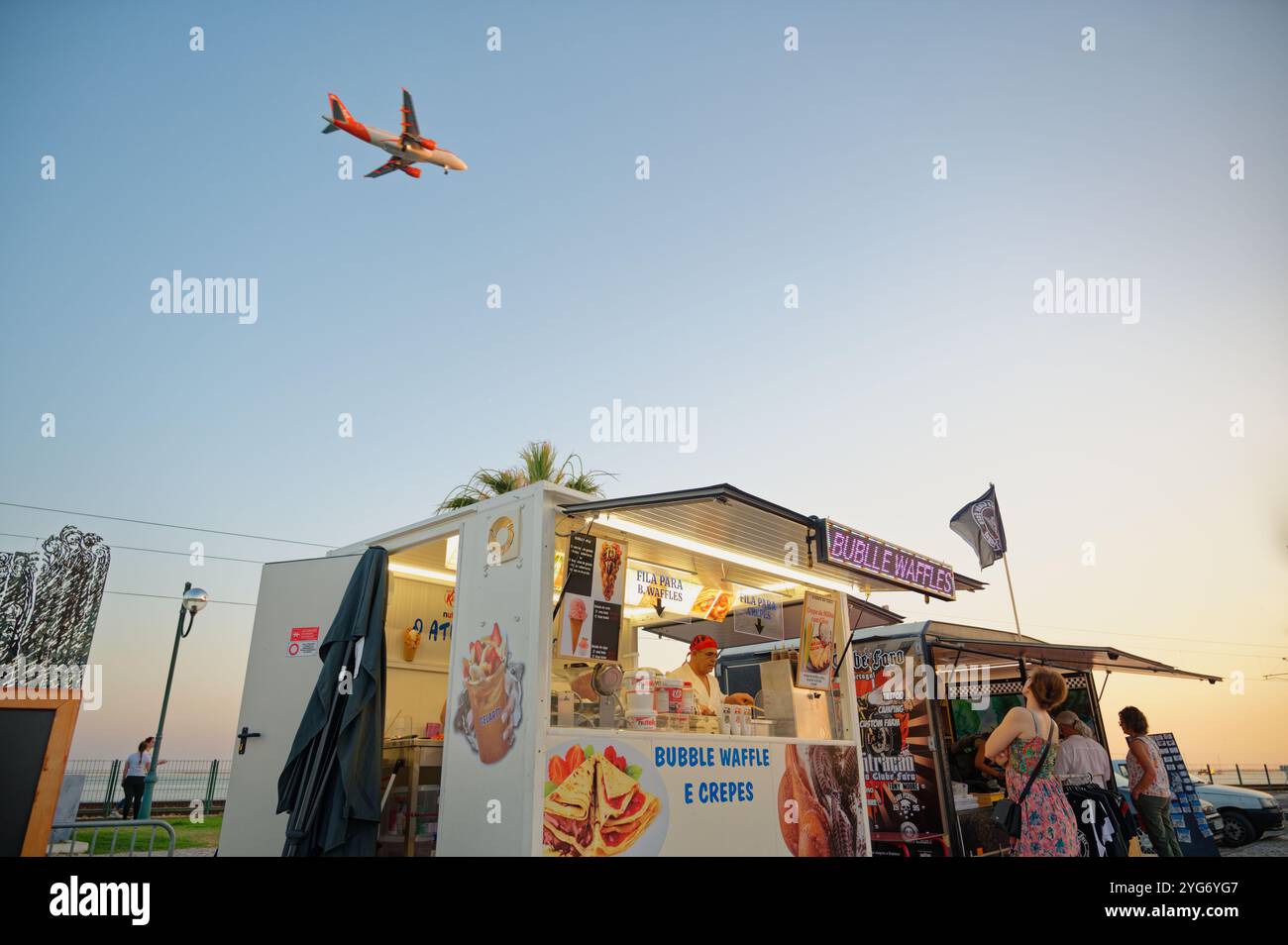 Chiosco di cibo che serve cialde e crepes sotto un cielo limpido mentre un aereo vola sopra la testa Foto Stock