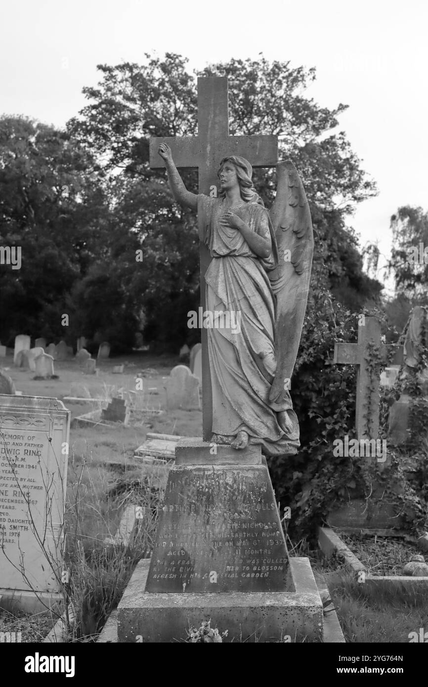 Highland Road Cemetery, Southsea, Portsmouth, Hampshire. 17 ottobre 2024. Scala di grigi, pietra commemorativa, c1937, per un ragazzo, e con una piccola piattaforma su cui si erge un angelo alato, con una croce dietro di lei. Foto Stock