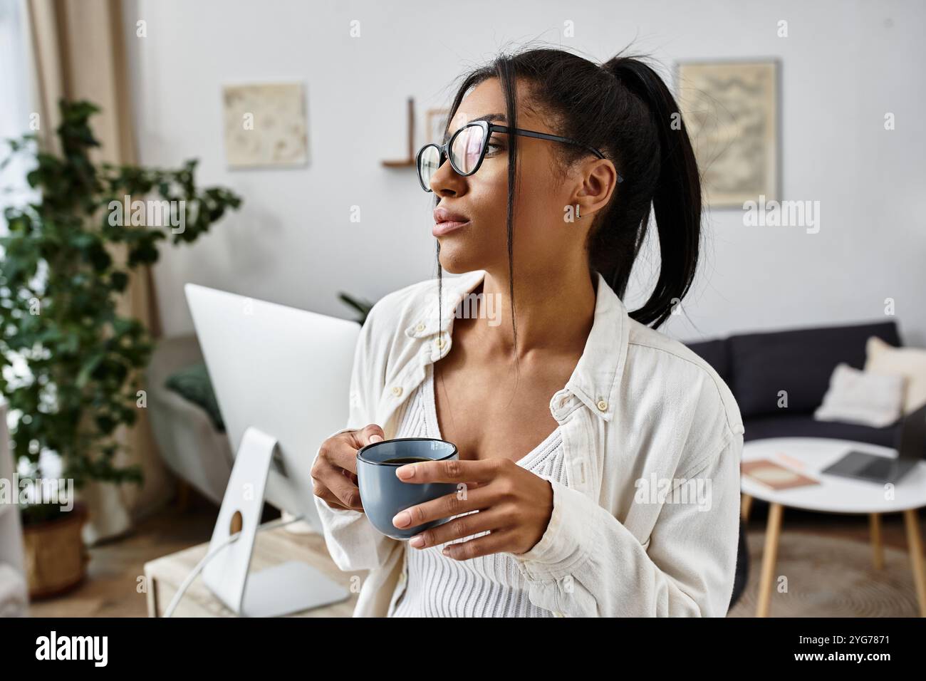 Una bella giovane donna tiene una tazza di caffè, concentrata sui suoi studi in un ambiente tranquillo. Foto Stock