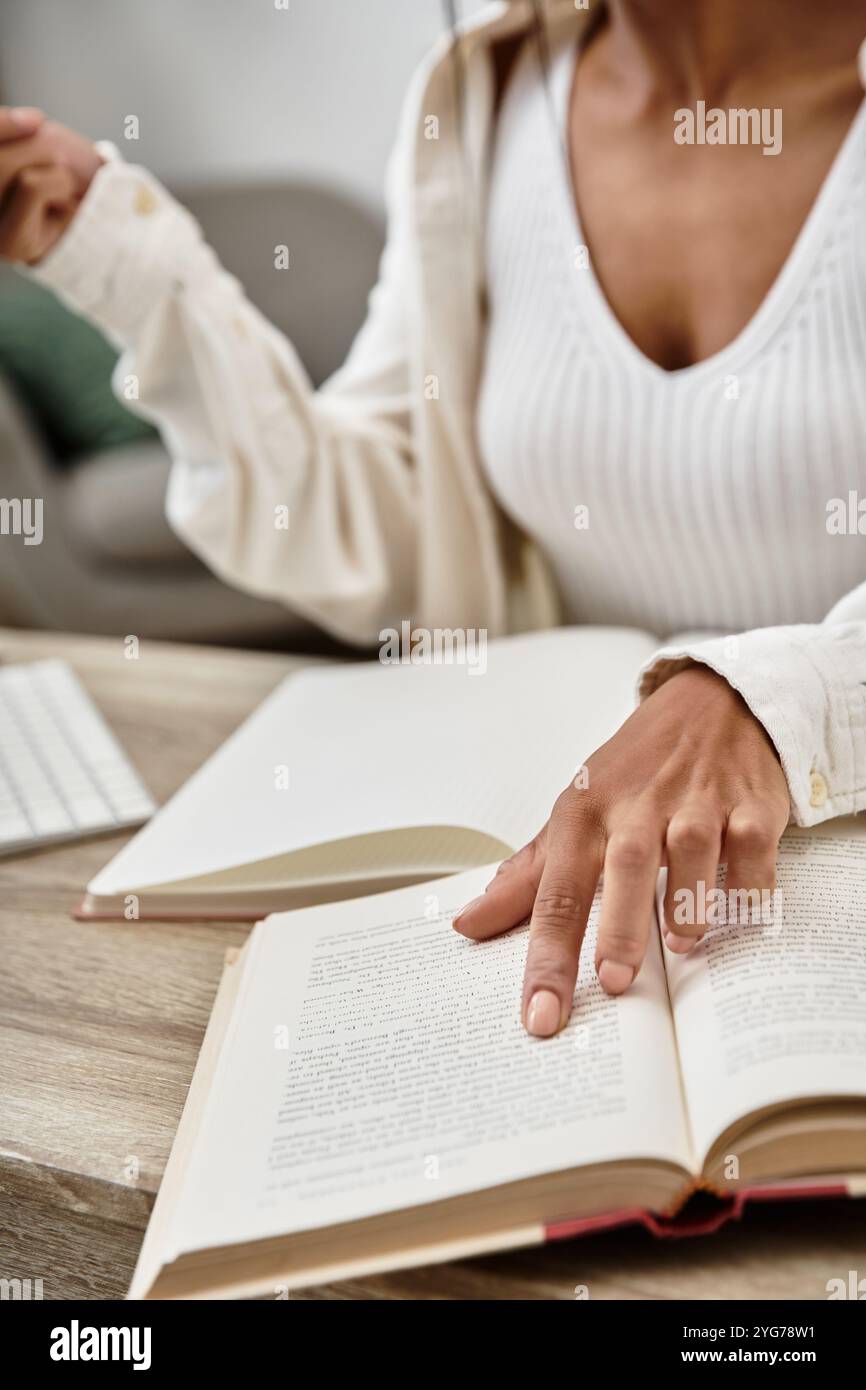 Una giovane donna studia intensamente a casa, girando le pagine del suo libro mentre è circondata dalla tecnologia. Foto Stock